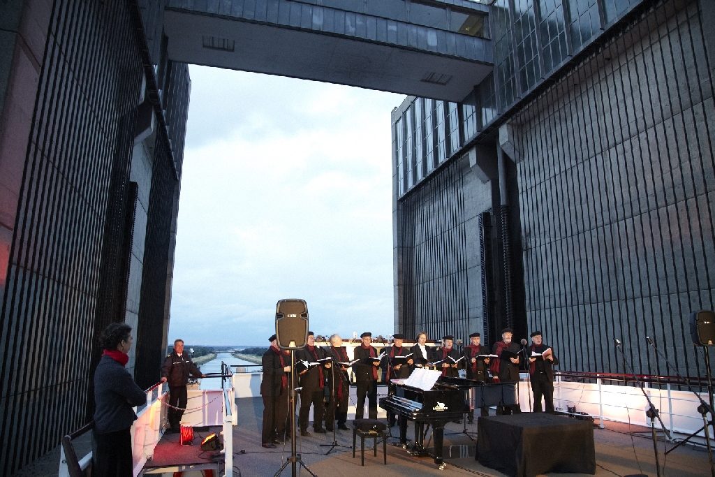 Ein Männerchor mit roten Schals singt auf dem Schiff, dahinter die hohen Wände des Hebewerks