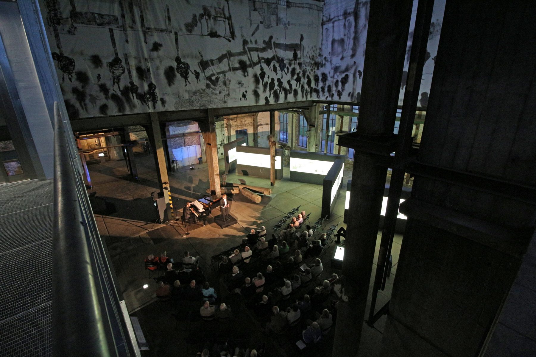 Blick von oben in das Kesselhaus: Publikum in Stuhlreihen vor dem Flügel zwischen Stahlträgern