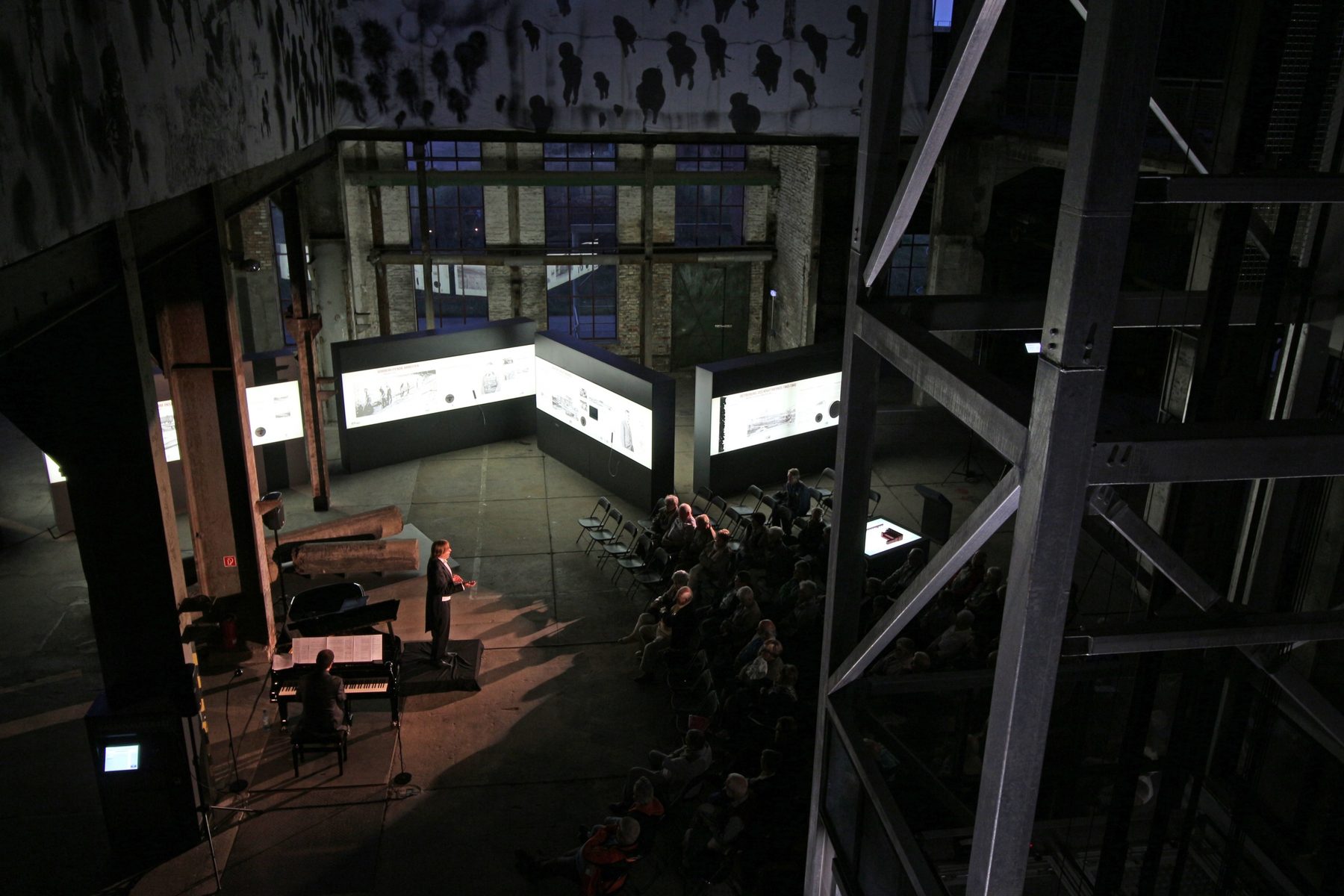 Blick von oben in die Halle: vorn ein Sprecher, dahinter beleuchtete Vitrinen und Zuhörer