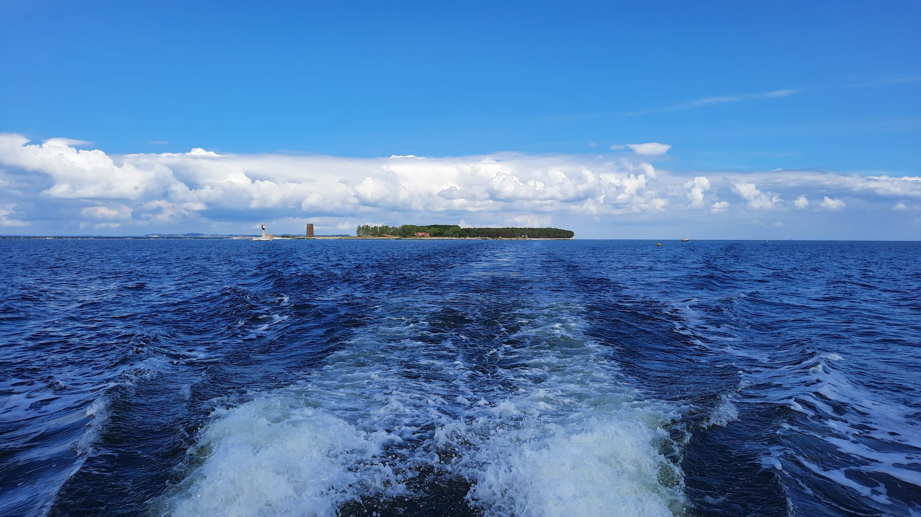 Das Kielwasser eines Schiffes auf der Ostsee, am Horizont eine flache Insel