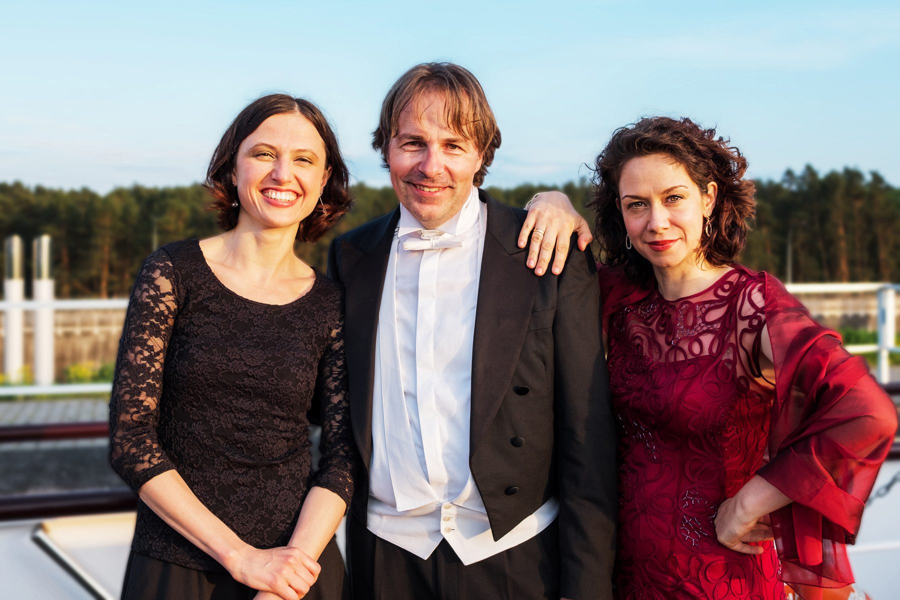Die Pianistin Alina Pronina, der Bariton Burkhard v. Puttkamer und die Sopranistin Barbara Berg stehen lächelnd nebeneinander auf dem Deck