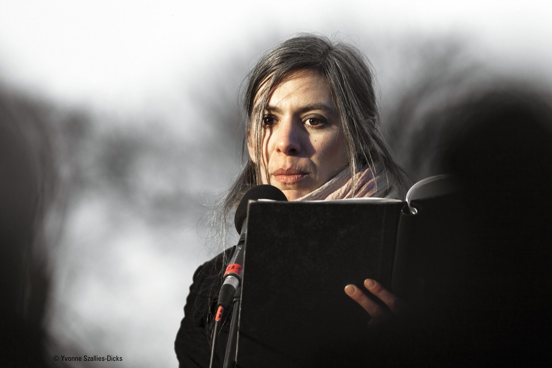 Eine Sprecherin mit aufgeschlagenem Buch am Mikrofon, im Gegenlicht