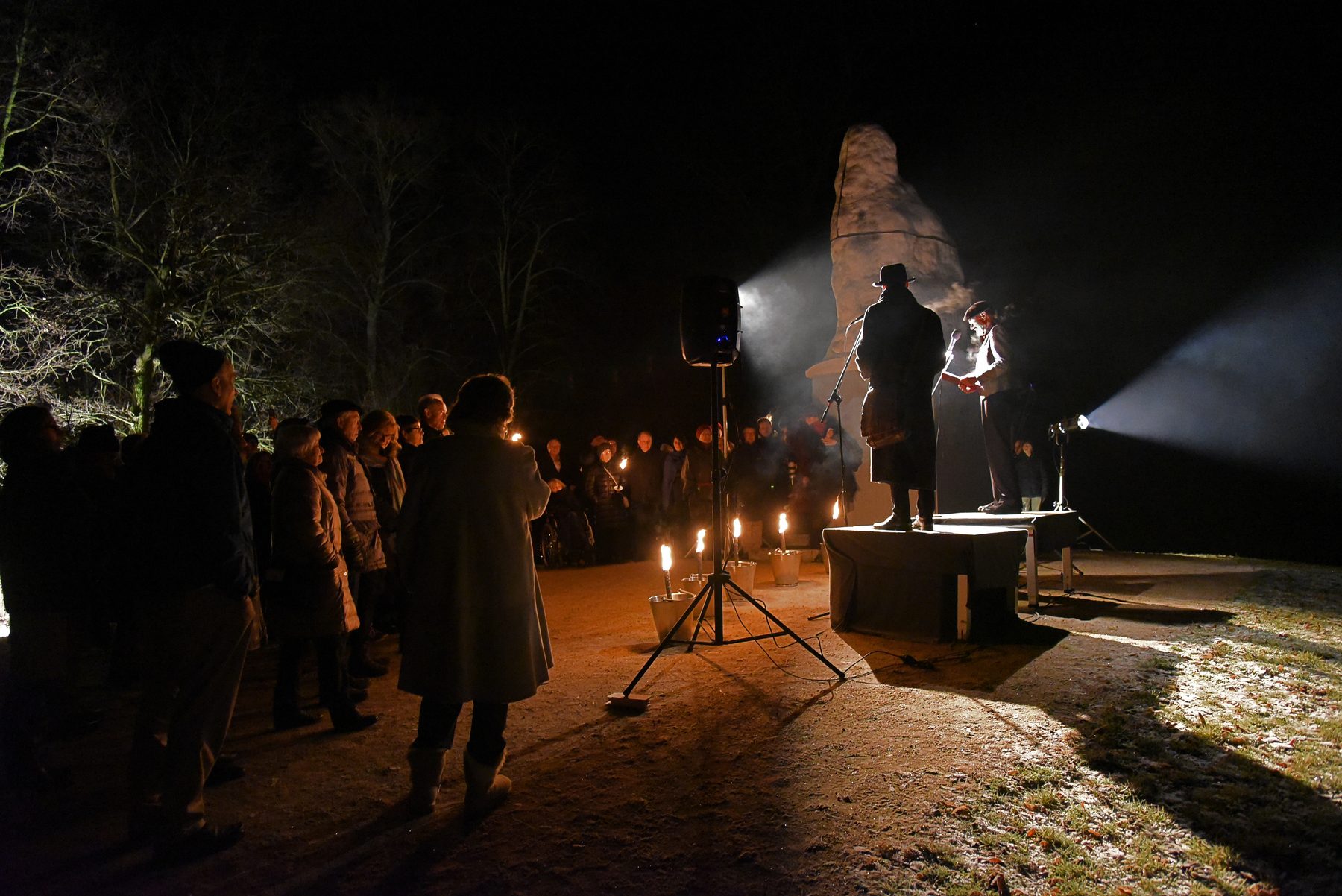 Nachts im Schlosspark: ein Sprecher auf einem Podest im Scheinwerferlicht, davor Zuhörer und Kerzen am Boden