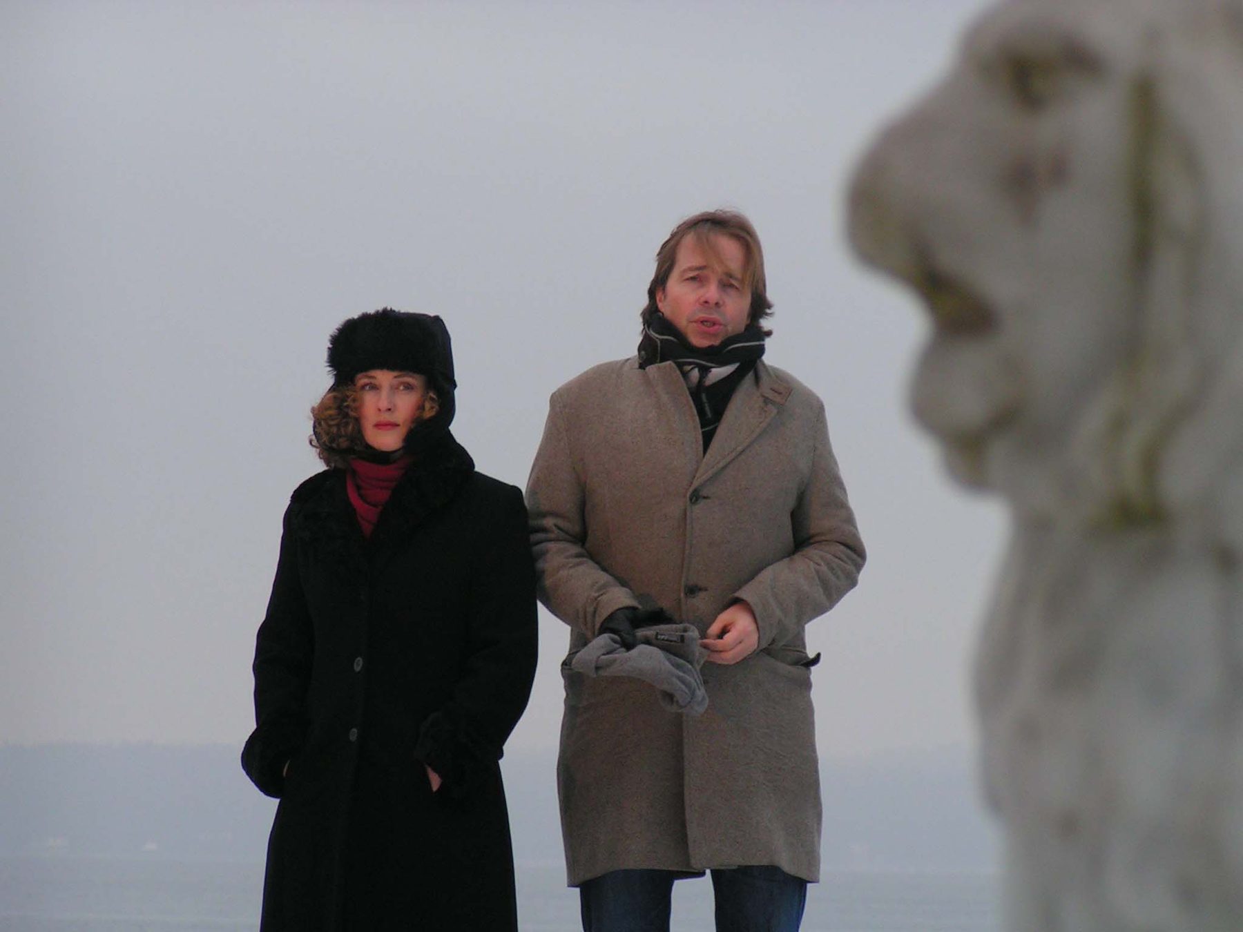 Zwei Menschen in Wintermänteln vor einer Löwenfigur im Nebel
